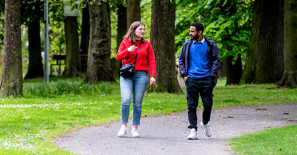 Een foto van twee mensen die wandelen in de natuur en met elkaar in gesprek zijn