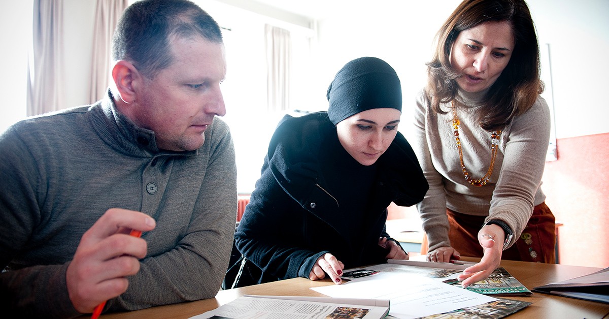 Een foto van drie mensen: twee mensen zitten neer en krijgen instructies van derde persoon die naast hen staat