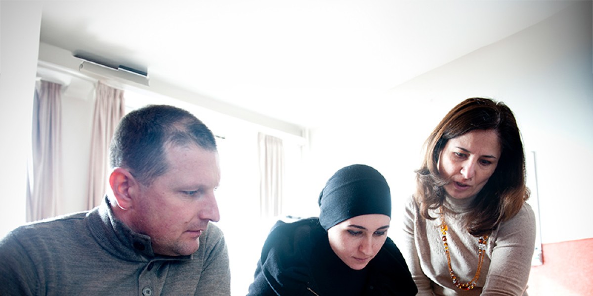 Een foto van drie mensen: twee mensen zitten neer en krijgen instructies van derde persoon die naast hen staat