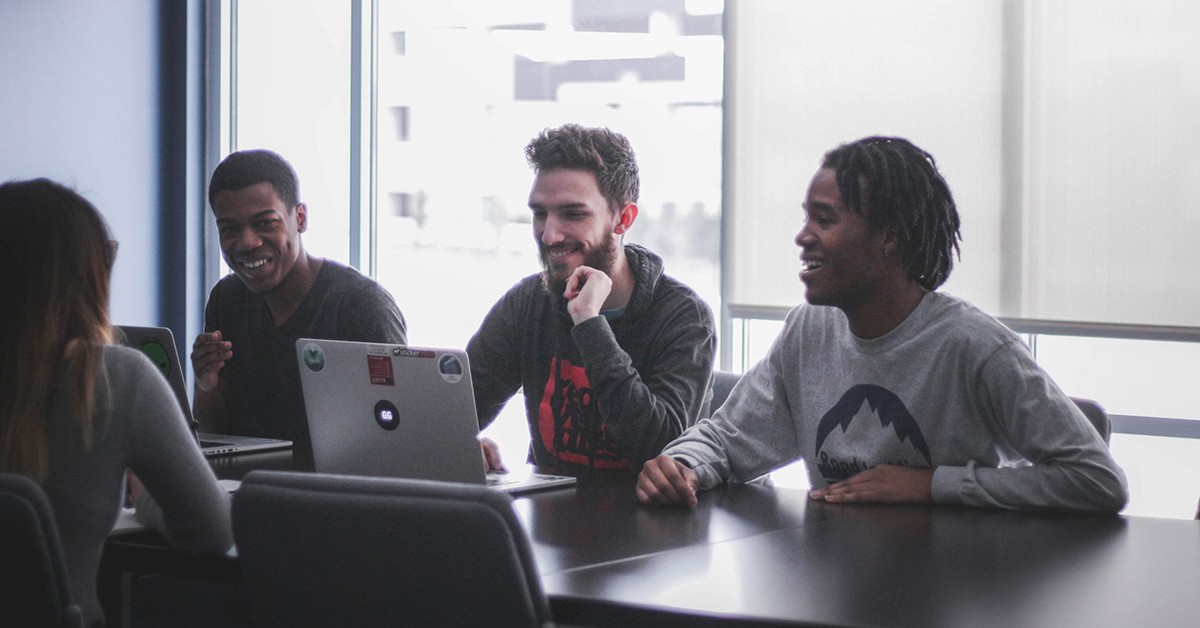 Foto van vier mensen in gesprek rond een tafel met één laptop